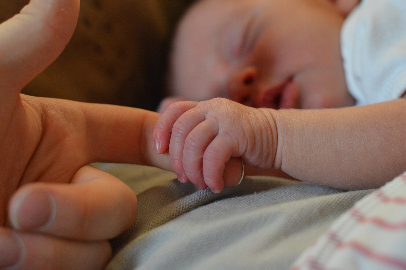 A newborn’s hand curled around an adult finger