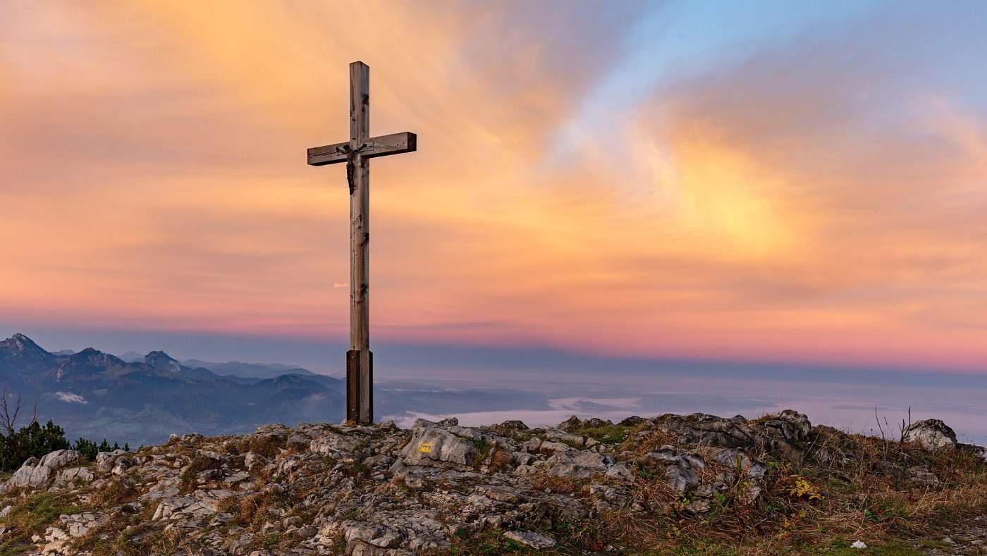 A wooden cross on a summit against an evening sky