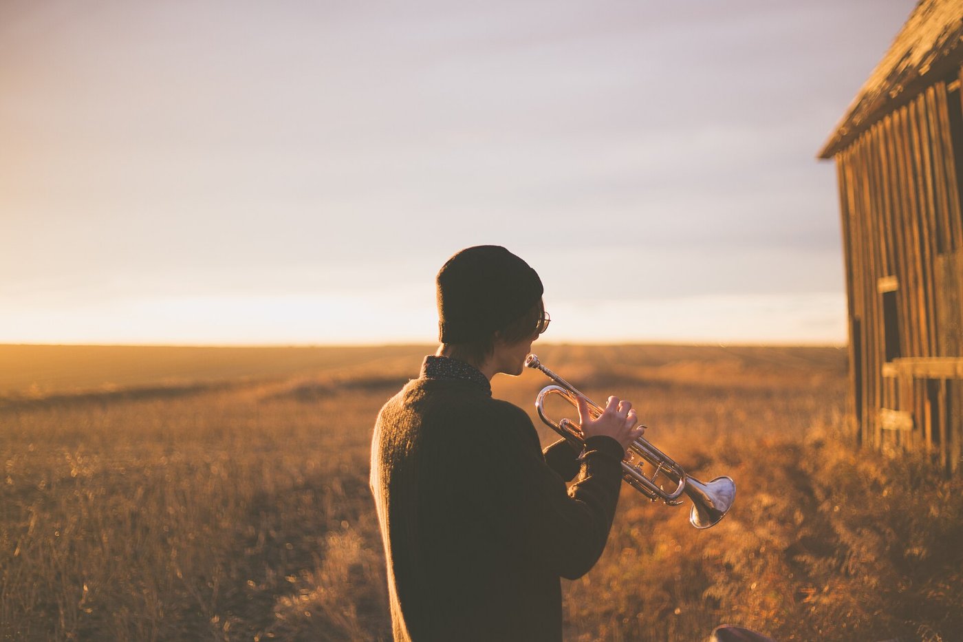 A trumpeter sounding across an open field at sunset